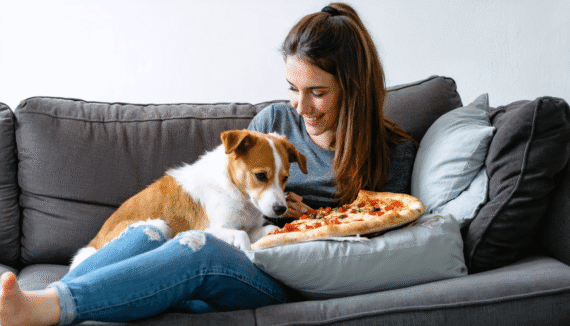 A Woman Cuddling with Her Puppy While Eating Pizza on the Couch